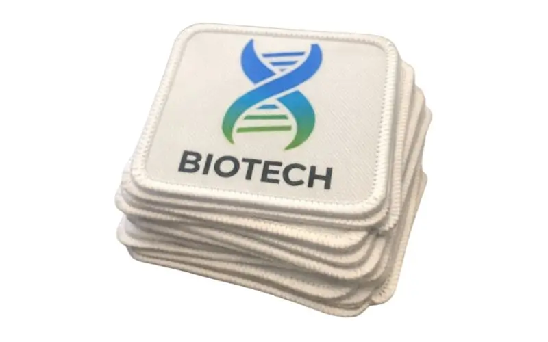 Stack of custom corporate patches with gradient logo for biotech firms.