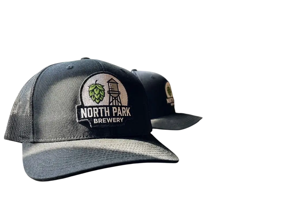 Two black trucker hats featuring custom embroidered North Park Brewery patches with a green hop and water tower design.