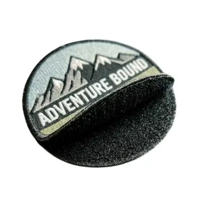 Close-up of an embroidered Adventure Bound patch being peeled away from its black hook-and-loop Velcro backing.