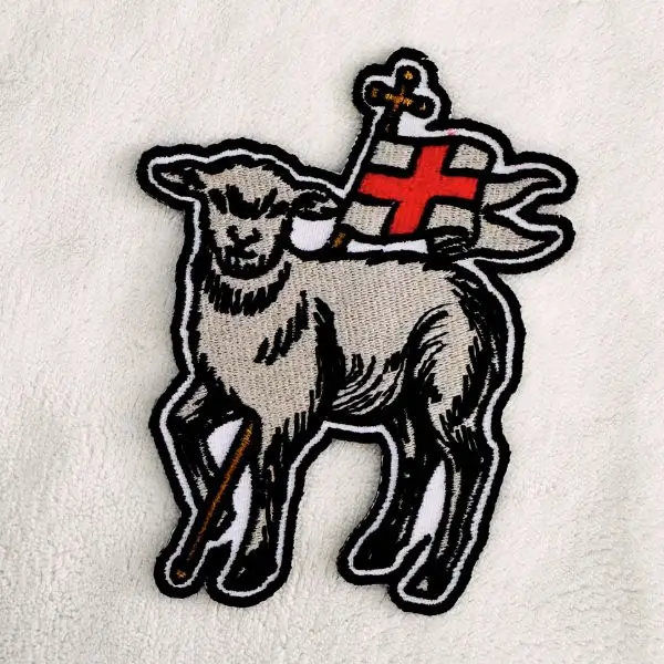 Die-cut embroidered lamb patch holding a red-cross flag with detailed monochrome stitching and black outline