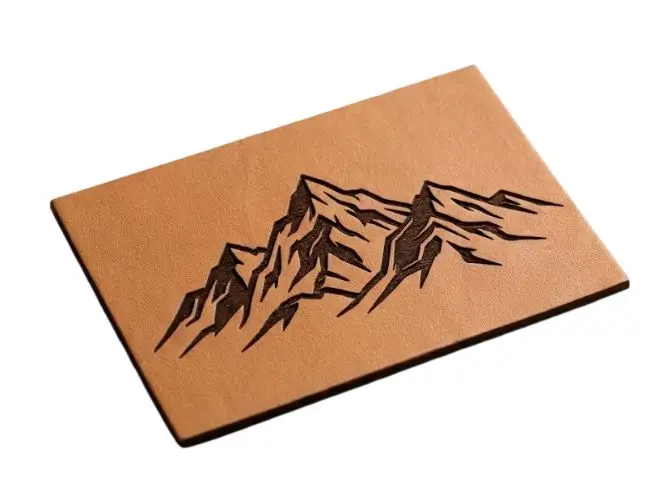 Laser-engraved leather patch with a dark charred mountain range design on light tan hide.