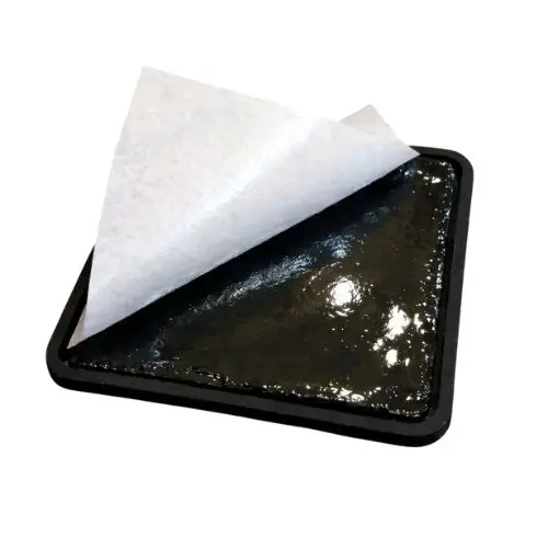 Rear view of a custom PVC patch with white wax paper being peeled back to reveal the sticky 3M adhesive layer.