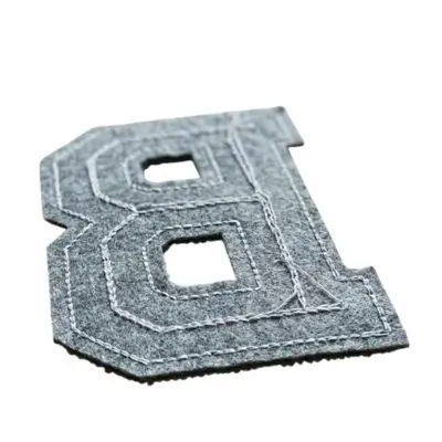 The reverse side of a varsity letter patch showing the reflective, glossy surface of industrial heat-seal iron-on backing.